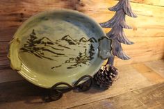 a green plate sitting on top of a wooden table next to a pine cone and tree