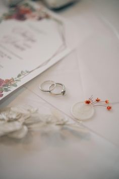 two wedding rings sitting on top of a table next to a brochure and some flowers