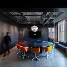 a large table with colorful chairs around it in an office space near a big window