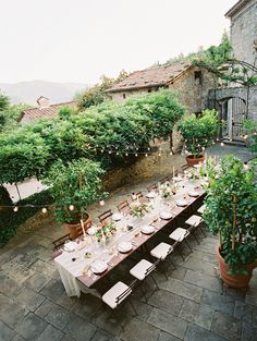 an outdoor dining table set up with place settings and greenery on the tables outside