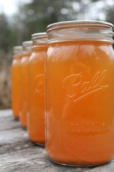 four jars filled with orange liquid sitting on top of a wooden table