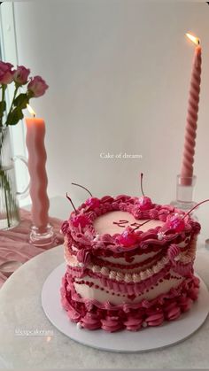 a pink cake sitting on top of a white plate next to a lit candlestick