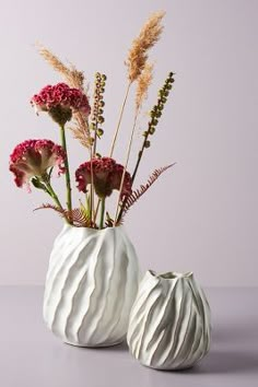 two white vases with flowers in them on a table