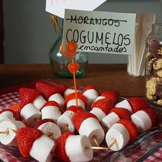 strawberries and marshmallows are arranged on skewers in front of a sign