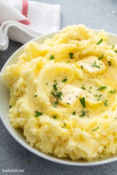 mashed potatoes with butter and parsley in a white bowl on a gray surface