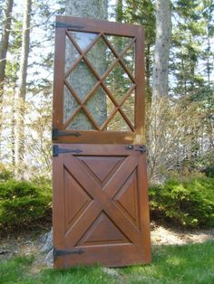 a tall wooden door sitting in the middle of a lush green field next to a tree