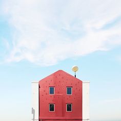 a red and white building with two windows on the roof, in front of a blue sky