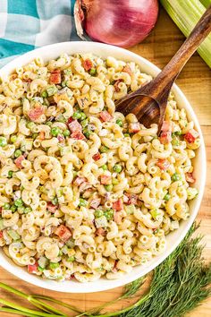 a bowl filled with macaroni salad next to an onion and celery