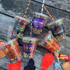 there are many halloween treats in plastic cups on the picnic table with candy sticks and candies