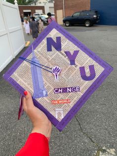 a person holding up a purple and white graduation cap with the words nyu change on it