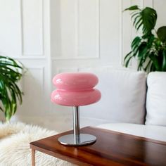 a pink lamp sitting on top of a wooden table next to a white couch and potted plant