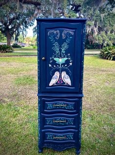 an ornate blue cabinet with two birds painted on the front and sides, sitting in grass