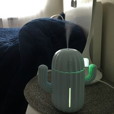 a green cactus humider sitting on top of a table next to a blue bed