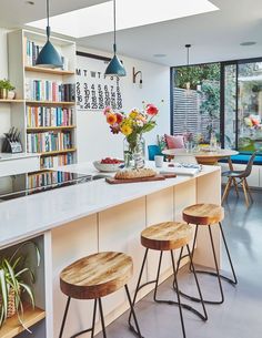 a kitchen with white counter tops and wooden stools in front of a book shelf filled with books