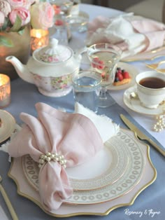 the table is set with pink and white dishes, silverware, and tea cups