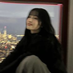 a woman sitting on top of a building next to a window with city lights in the background