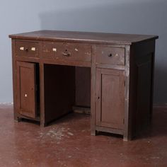 an old wooden desk with two doors and drawers on the top, in front of a gray wall