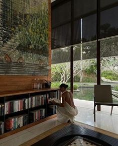 a woman sitting on the floor in front of a bookshelf reading a book