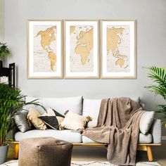 three framed maps hang on the wall above a couch in a living room with potted plants