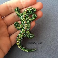 a small green lizard brooch with pearls on it's tail, sitting in someones hand