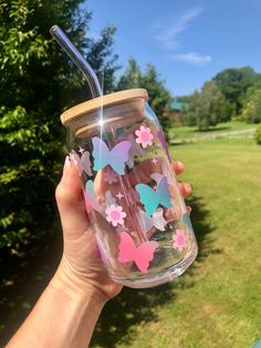 a person holding up a glass with butterflies on it and a straw in their hand