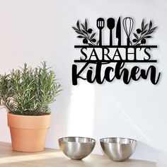 a metal sign with the words sara's kitchen on it next to two bowls and a potted plant