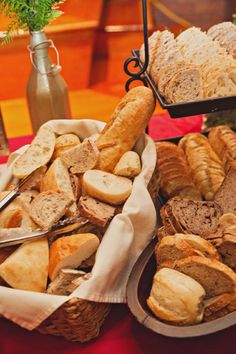 breads and pastries are displayed in baskets on a red tableclothed cloth