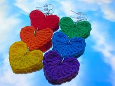 four crocheted heart shaped earrings hanging from hooks on a blue sky with clouds in the background