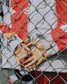 a close up of a person behind a chain link fence holding their hands on his chest