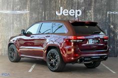 a red jeep parked in front of a building with the jeep logo on it's side