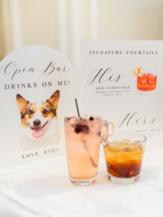 two cocktails are sitting on a table next to a sign with an image of a dog