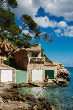 a man standing on the rocks next to some buildings by the ocean with blue sky and clouds