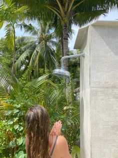 a woman standing next to a shower head in a lush green jungle area with palm trees