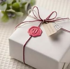 a present wrapped in white paper with a red wax stamp on it and tied around the edge