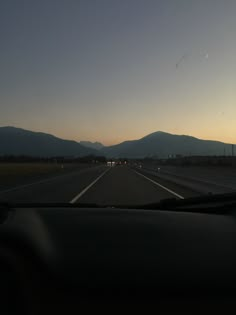 the sun is setting on an empty highway with mountains in the distance and cars driving down it