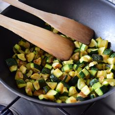 a pan filled with chopped zucchini next to a wooden spoon on top of a stove