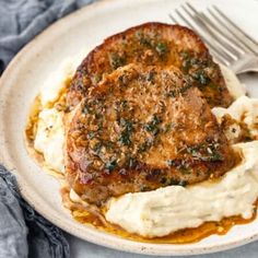 two meat patties with mashed potatoes on a white plate next to a fork