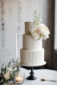 a three tiered white wedding cake with flowers on top and candles next to it