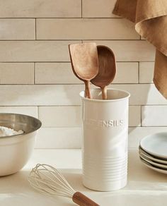 a white can with wooden spoons in it next to some plates and utensils