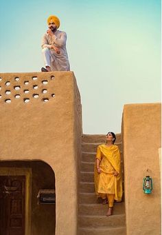 two men dressed in yellow standing on the top of a building with steps leading up to it