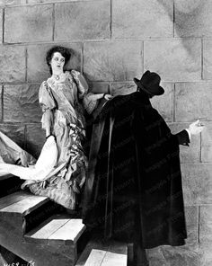 an old black and white photo of two women dressed in costumes sitting on steps with one woman leaning against the wall