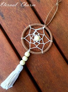 a white beaded dream catcher hanging on a wooden table with the words essential charm written above it