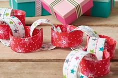 several different colored boxes and ribbons on a wooden table with one wrapped in wrapping paper