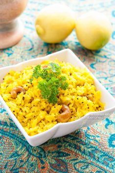 a bowl filled with yellow rice next to two lemons on a blue and white table cloth