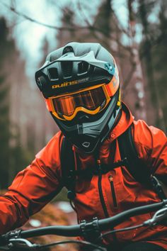 a man in an orange jacket and helmet riding a bike through the woods on a cloudy day