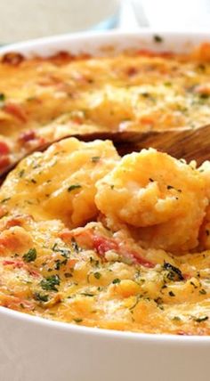 a casserole dish with shrimp and cheese in it is being spooned into the casserole