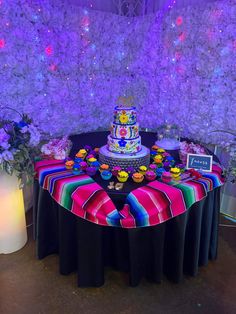 a table topped with a colorful cake and cupcakes