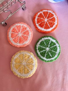 three crocheted fruit coasters sitting on top of a pink tablecloth next to a wire rack