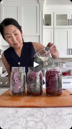 a woman pouring water into jars filled with vegetables