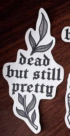 two stickers that say dead but still pretty on a wooden table with writing in black and white